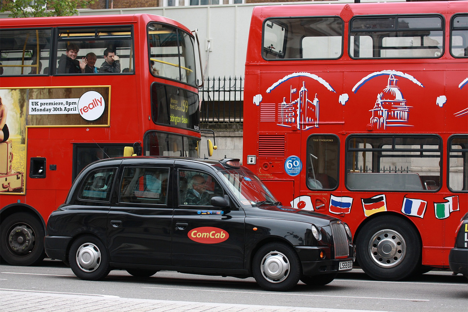 black British taxi in front of two double-decker buses