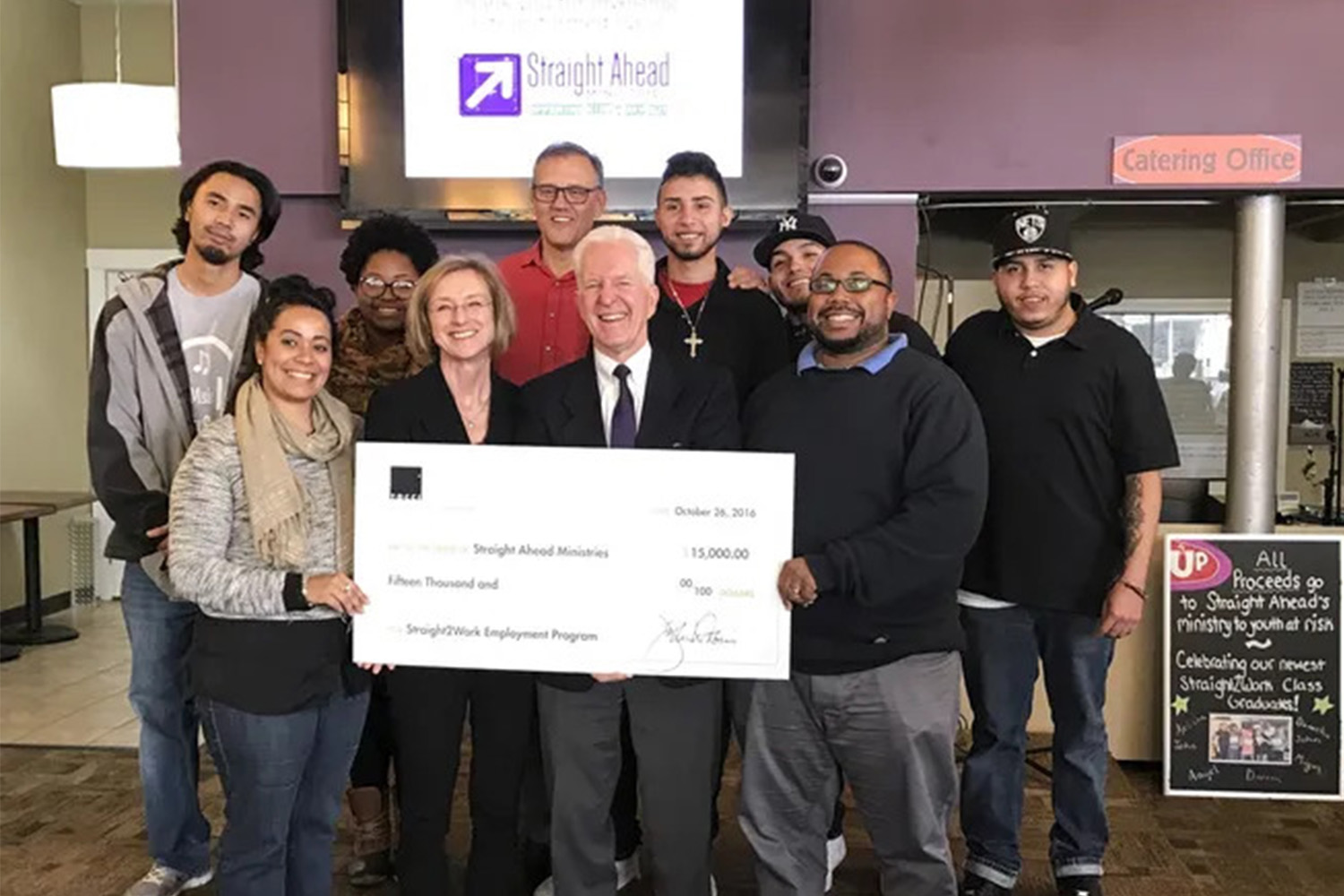 John and Lila Tocci donate $15,000 to Straight Ahead Minstries, a Worcester-based non-profit. They stand at the front of a group, holding a large check.