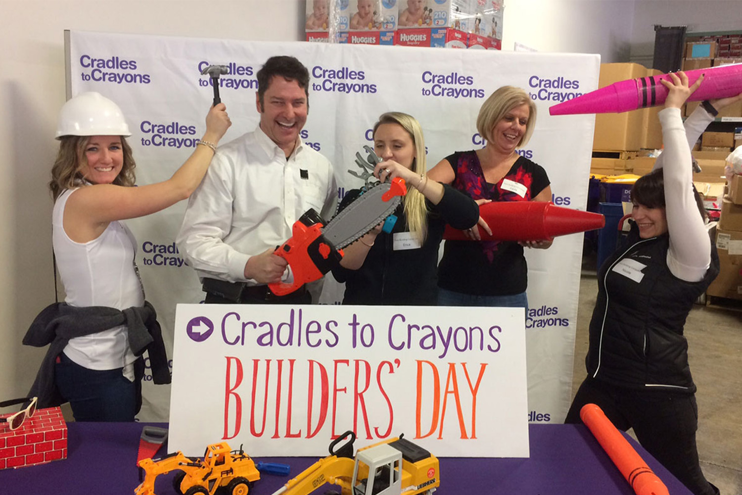 Staff hold large plastic crayon props after a successful Builder's Day at Cradles to Crayons