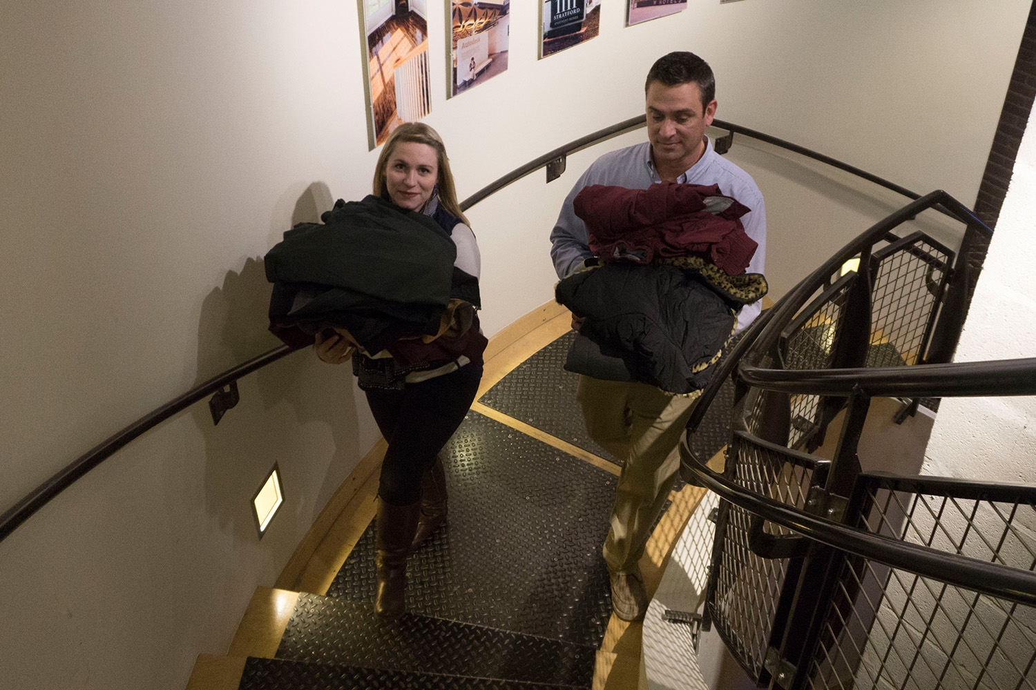 Two Tocci staff members walk up the stairs carrying coats for a coat donation drive