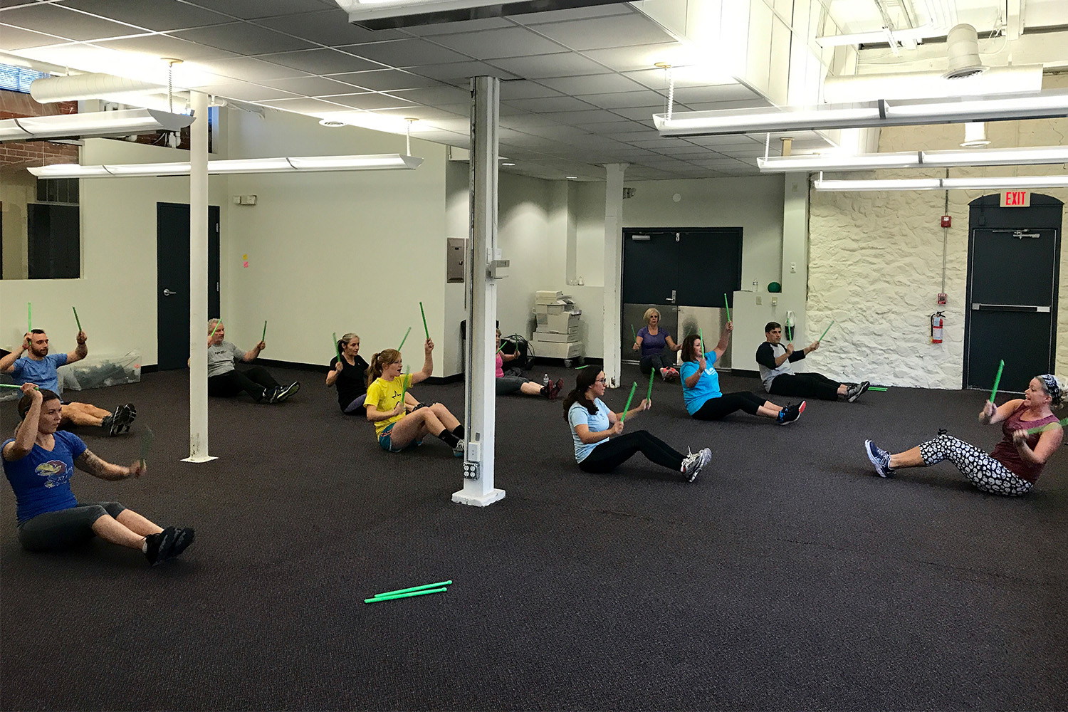 Ten people sit on the ground in a pose during a pound fitness class