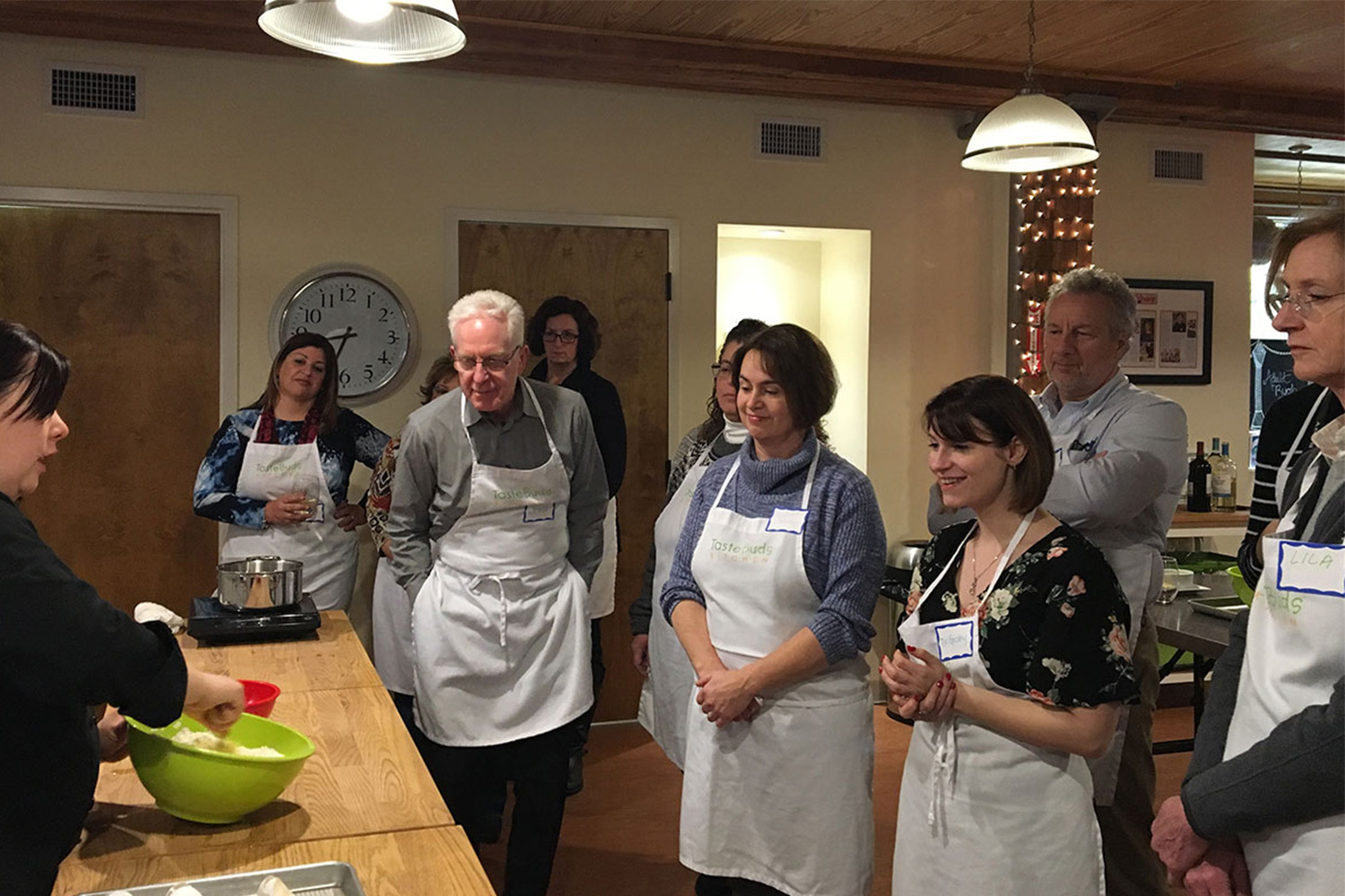 John Tocci, Lila Tocci, and other staff members gather around an instructor teaching the group how to make pasta