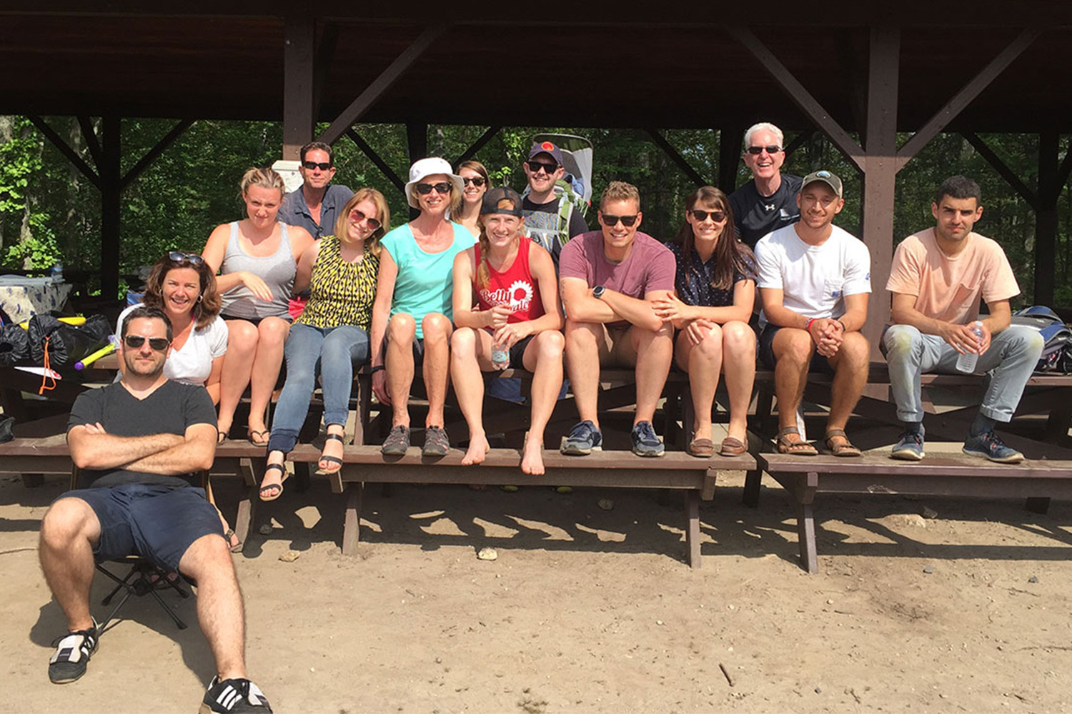 Group of Tocci staff sitting under a wooden overhang during a summer barbeque