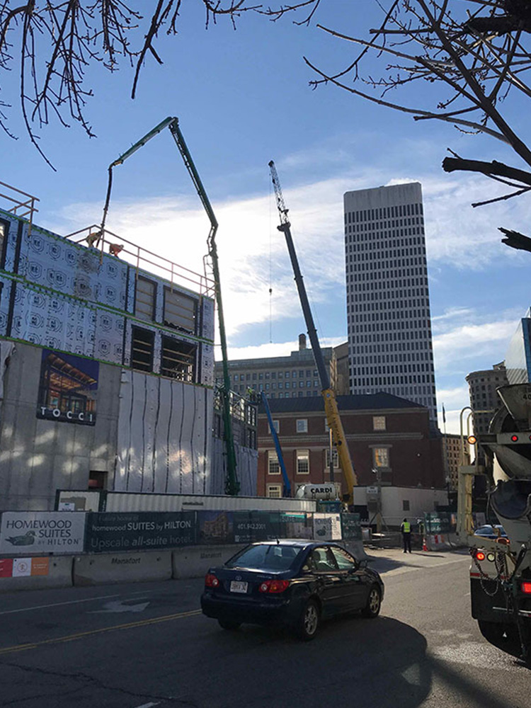 Street view of progress at Providence Hilton Homewood Suites. The site is blocked by concrete barricades, but one can clearly see the cranes lifting above the jobsite.