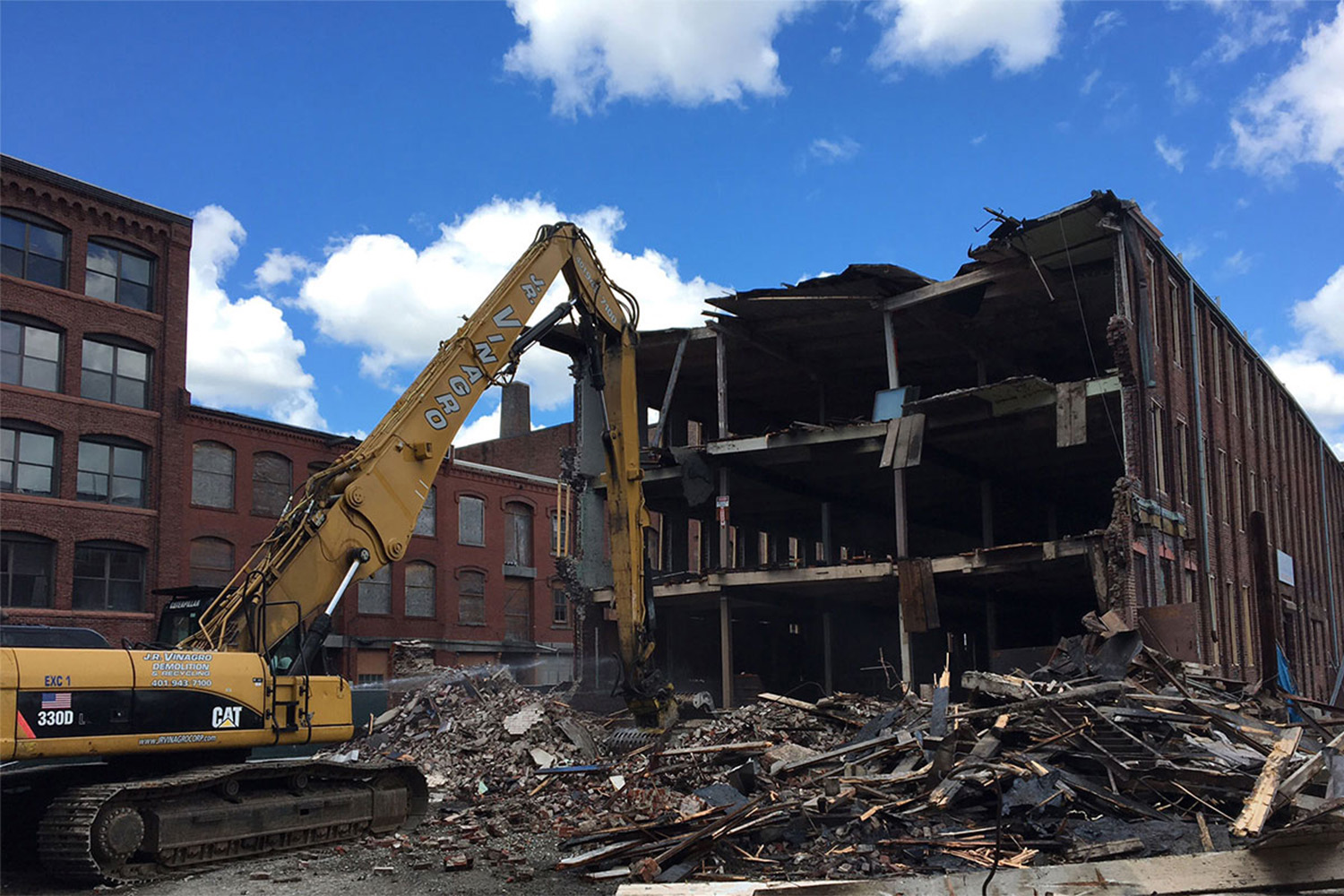 Demolition excavator in front of partially destroyed red brick building
