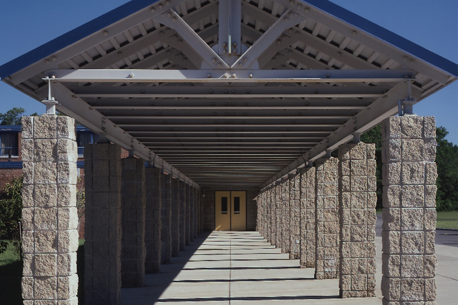 Long walkway leading to main entrance, with roof above and pillars on the sides 