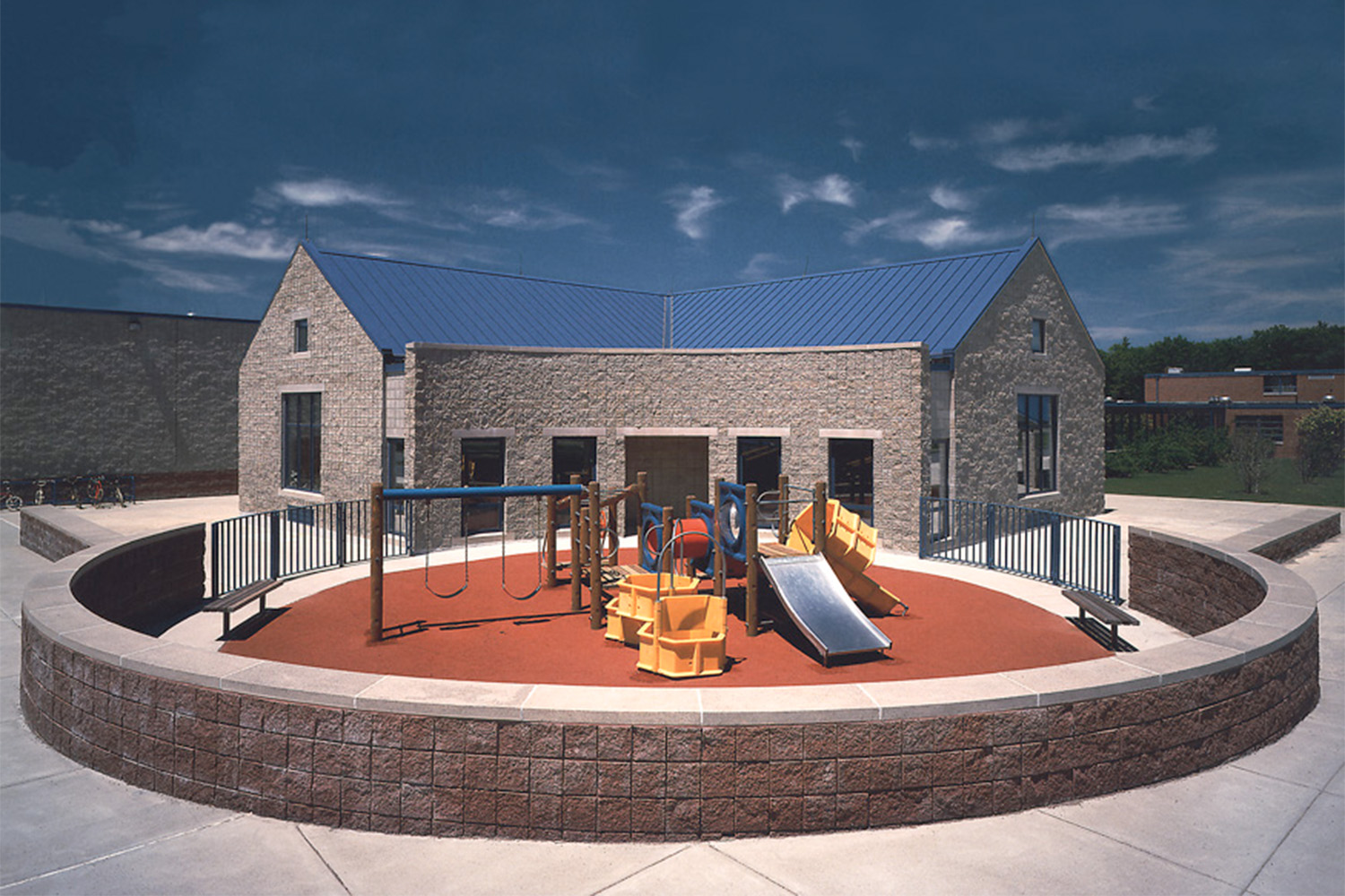 Kids playground with swing set and slides, with brick wall surrounding the playground