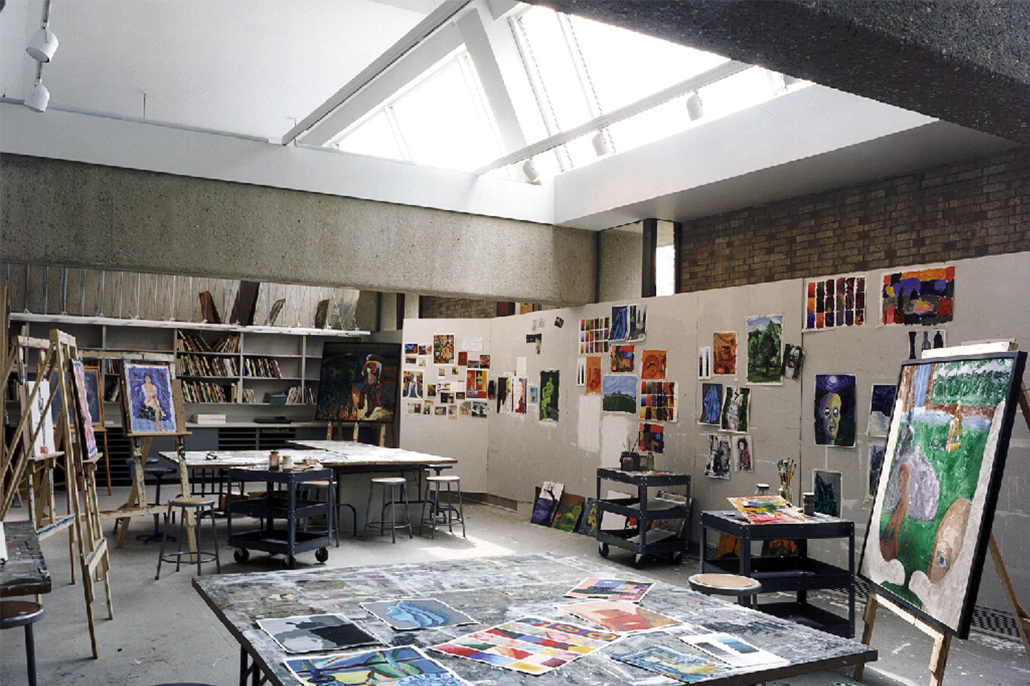 Painting studio with window on ceiling, various paintings and art books in bookshelf