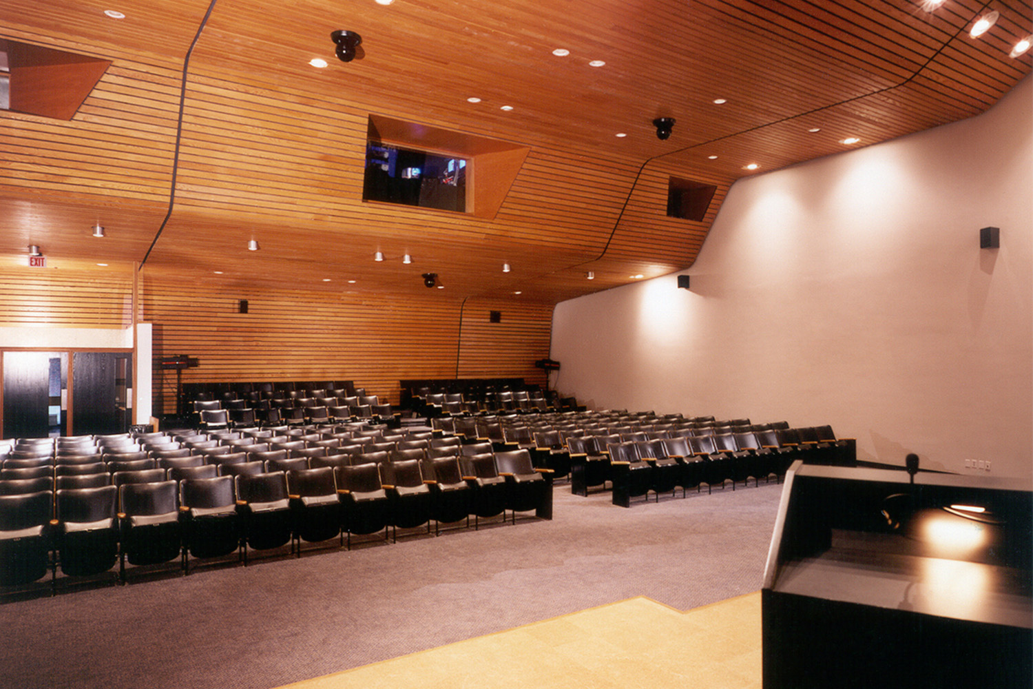 Large auditorium, with wooden ceiling, and light fixtures on either side 