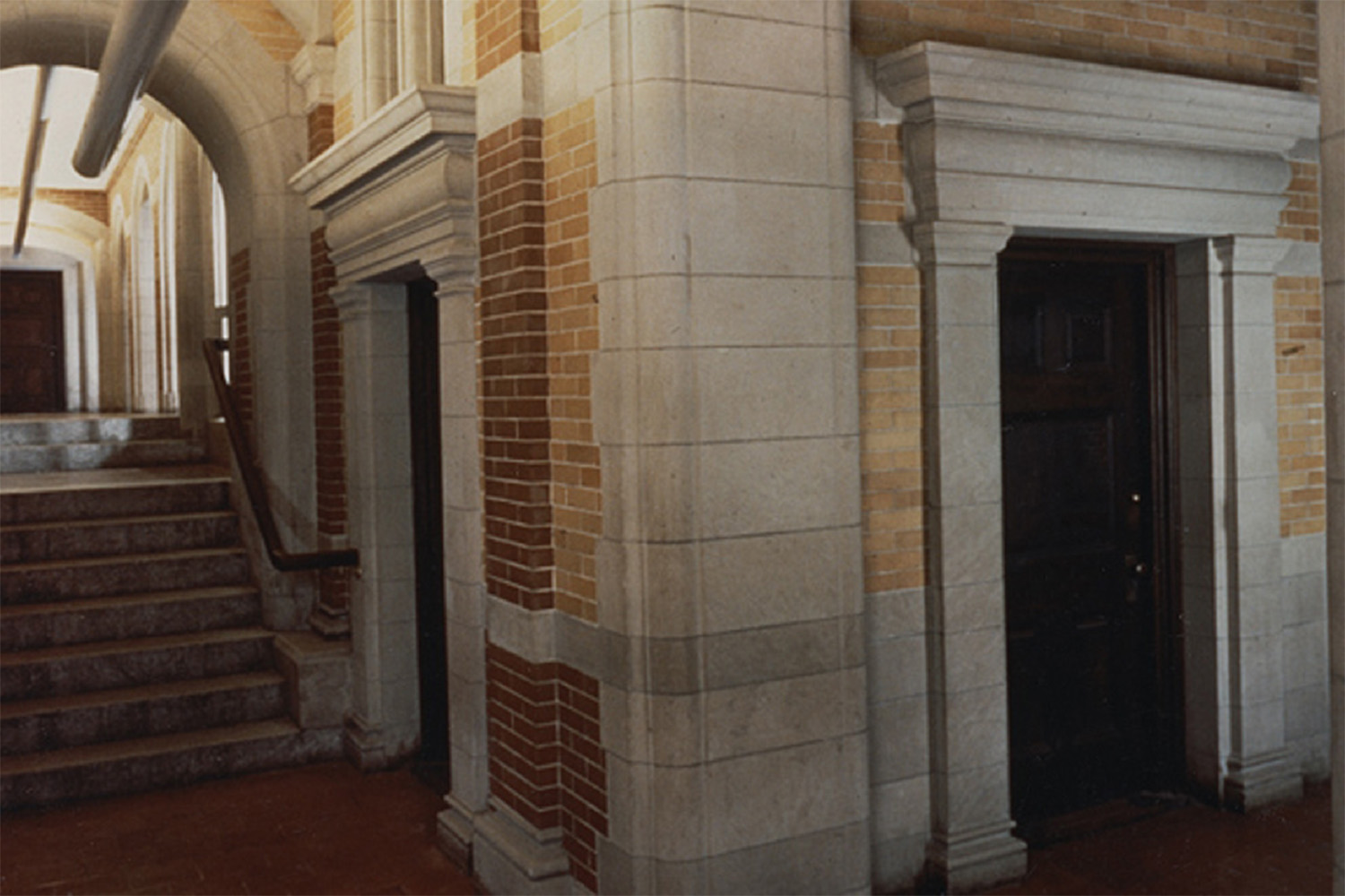 Concrete arched hallway beside brick wall with entryways, which have concrete frames 