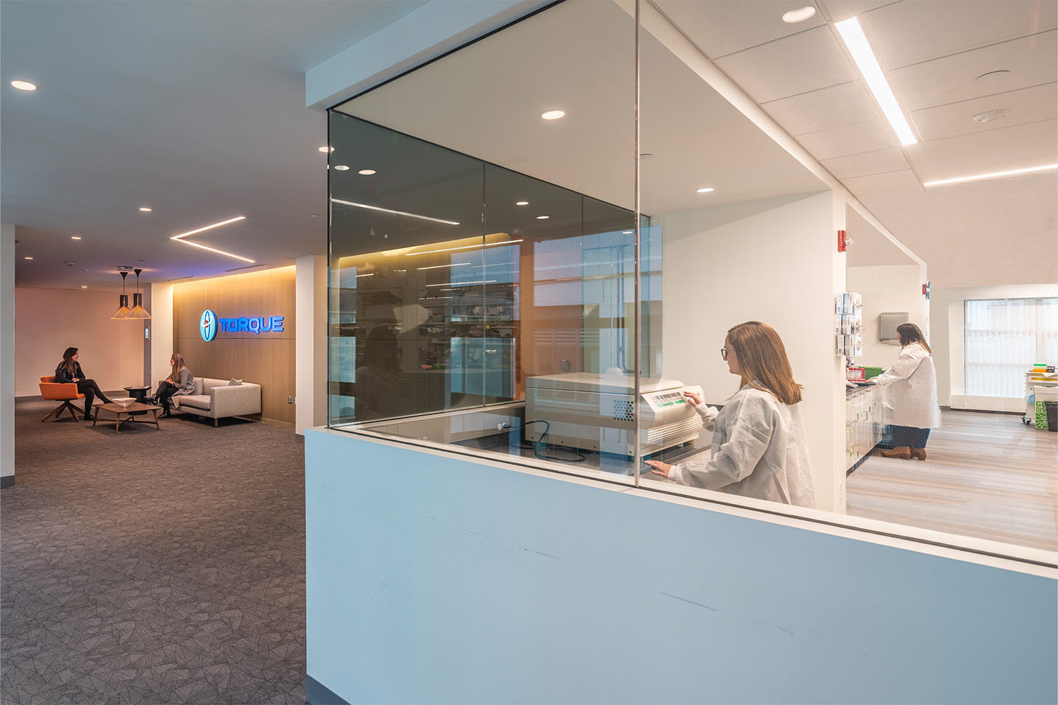 Lobby next to room with glass walls, and a woman using a chemical processer inside