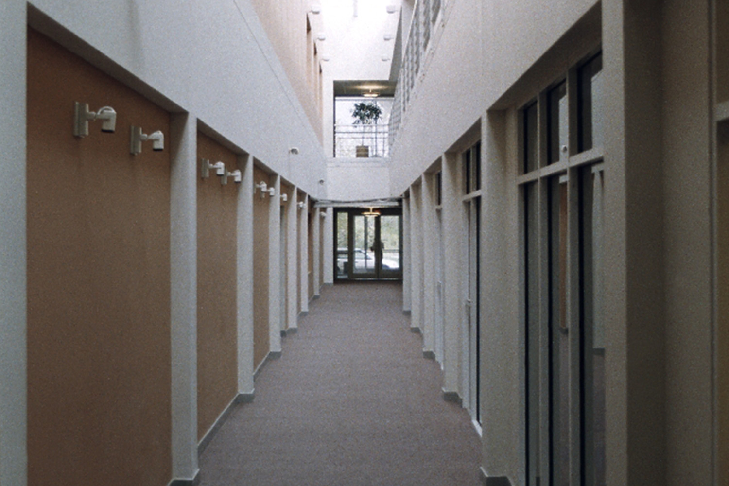 Hallway with building exist at the end, and multiple doors to the left and right 