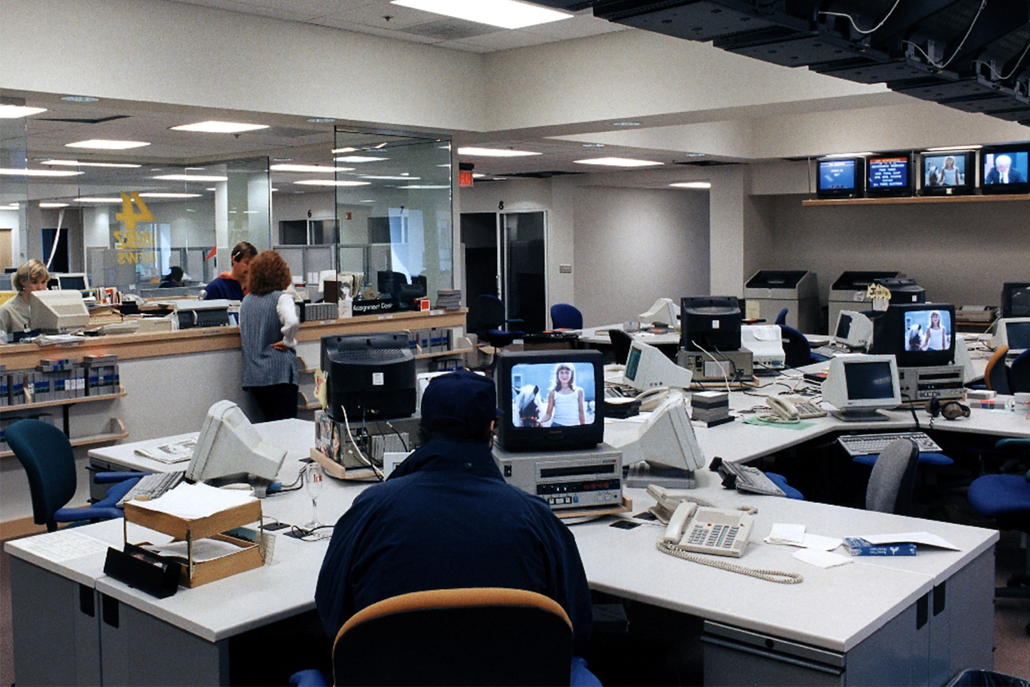 Newsroom with multiple TV's, and people working at desks 