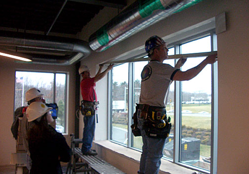 2 construction workers measuring length of window 