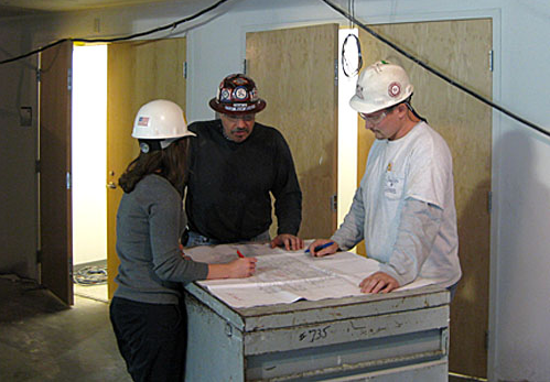 3 construction workers in hard hats overlooking blueprints