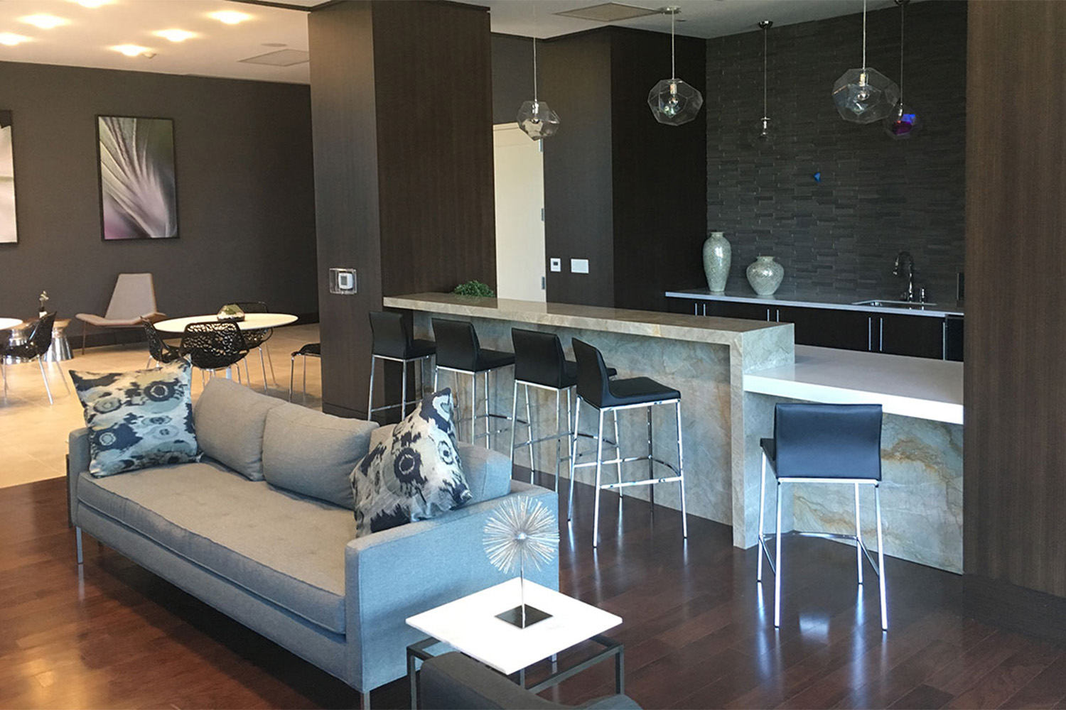 Plush grey couch in front of bar table and chairs, next to lobby room
