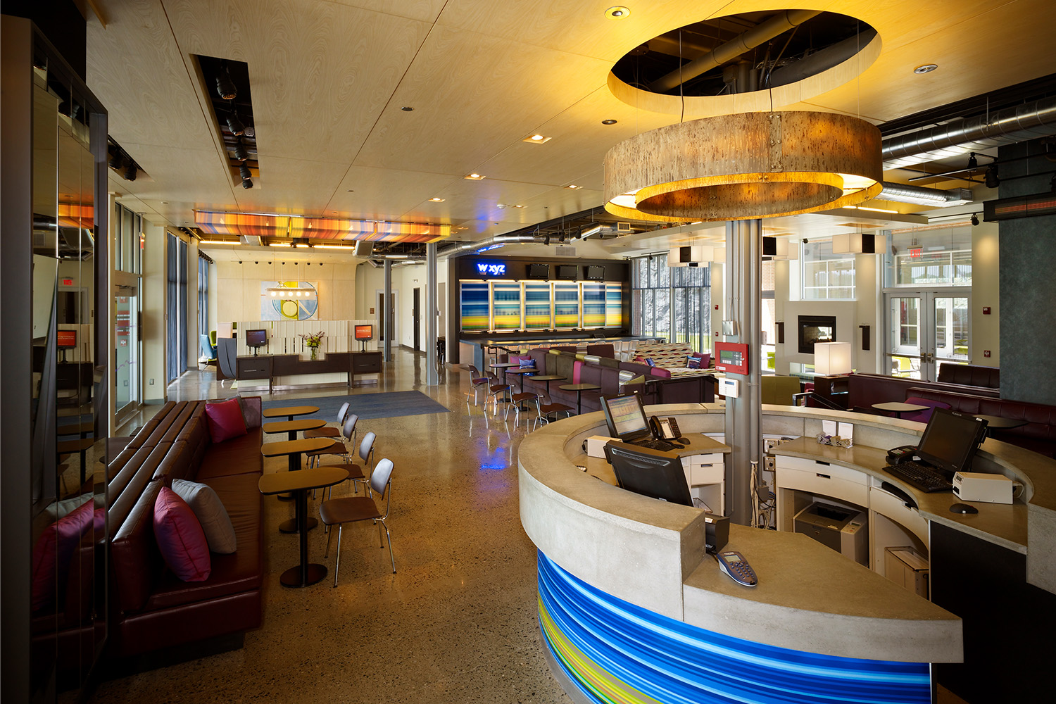 View of lobby area from behind receptionist desk: maroon chairs and long couches, and wooden ceiling with circular light fixtures 