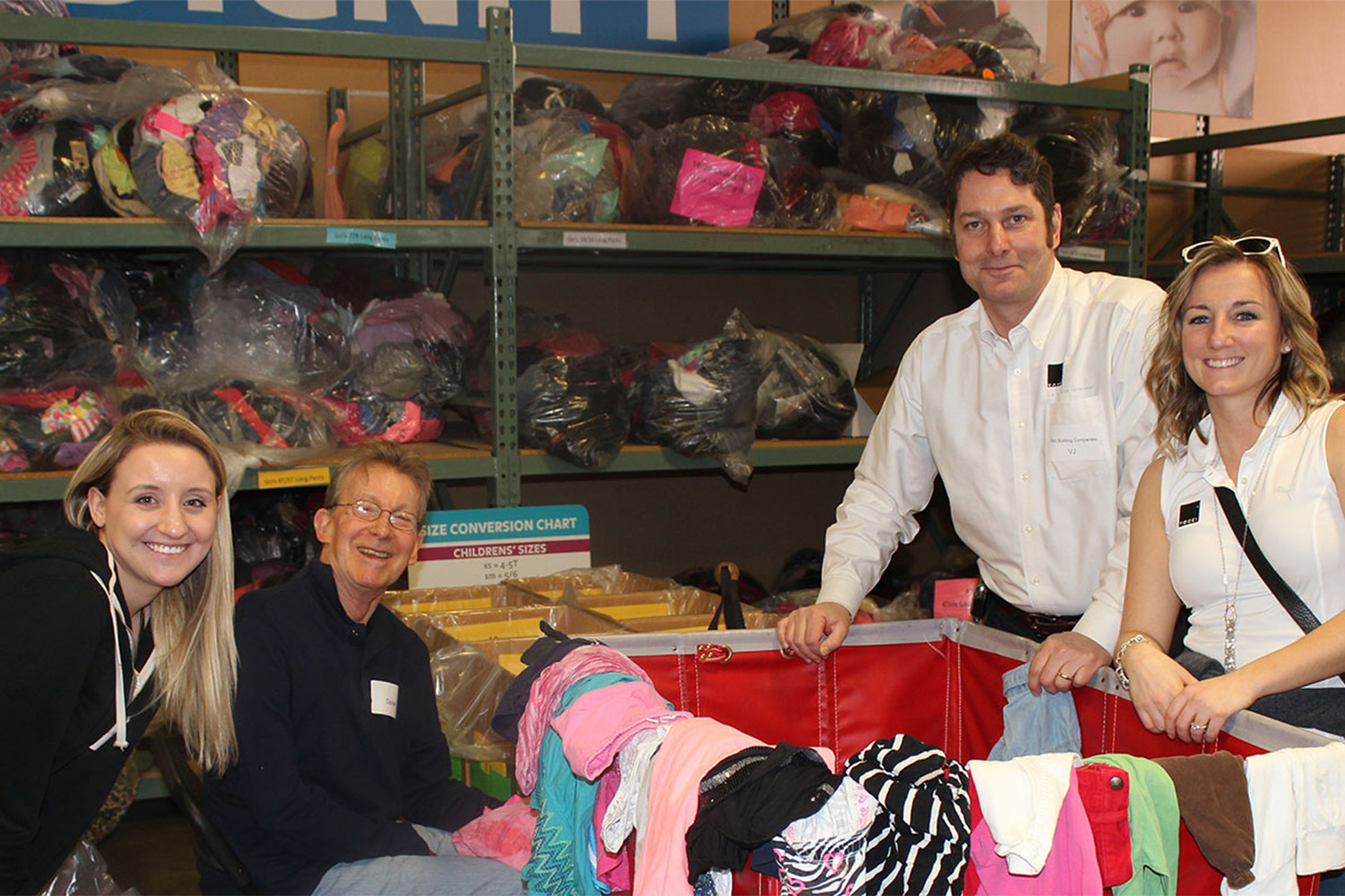 4 people standing around Cradles-to-crayons donation bin