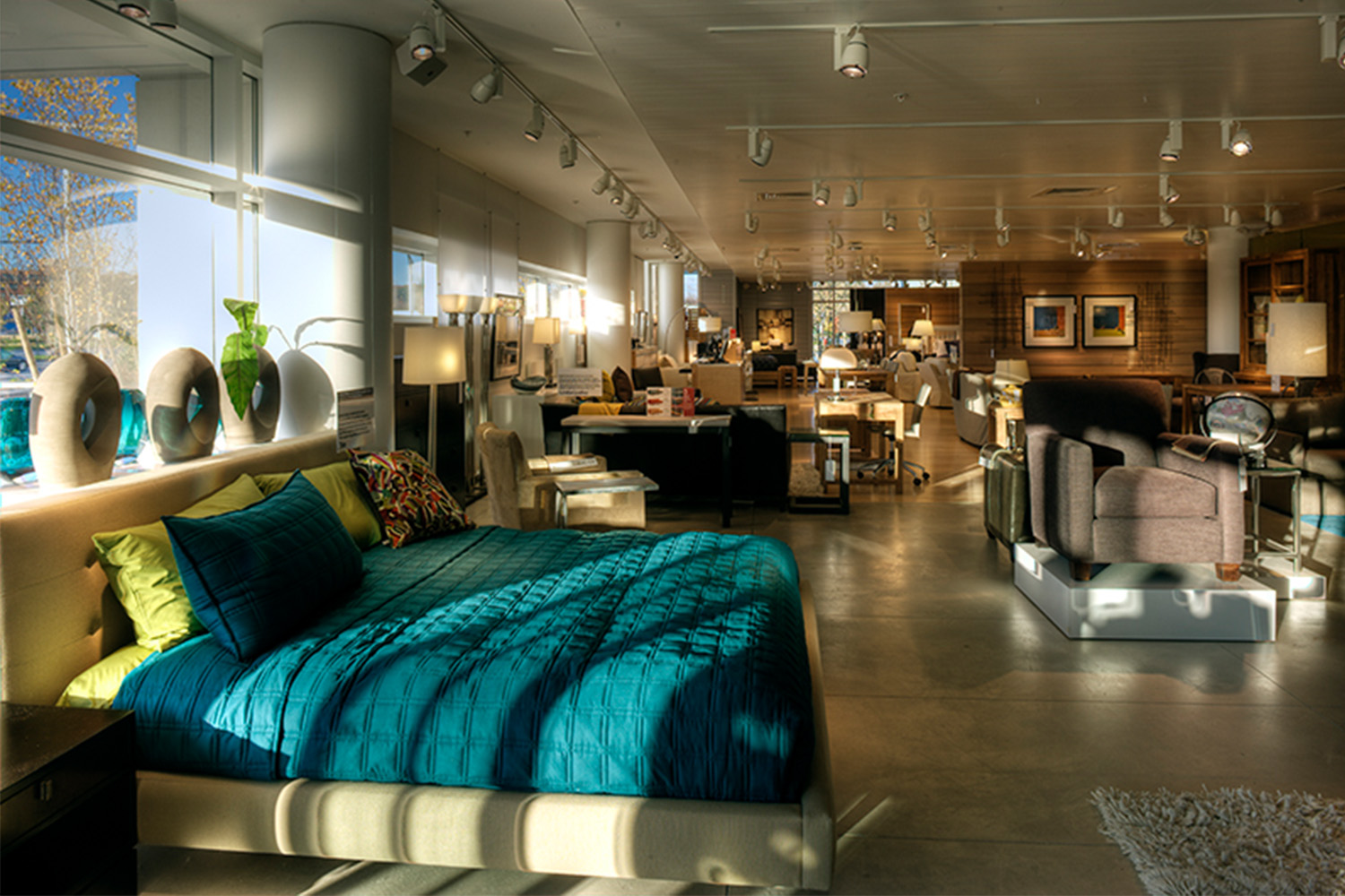 Store merchandise consisting of a bed with teal bedsheets, artistic vases, a brown chair, a couch, etc.