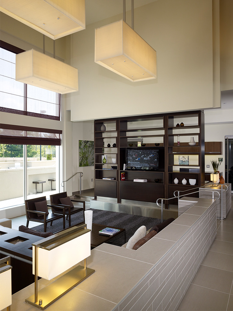 Lobby area with rectangular light fixtures, wooden shelf and chairs, and large widows allowing subtle lighting 