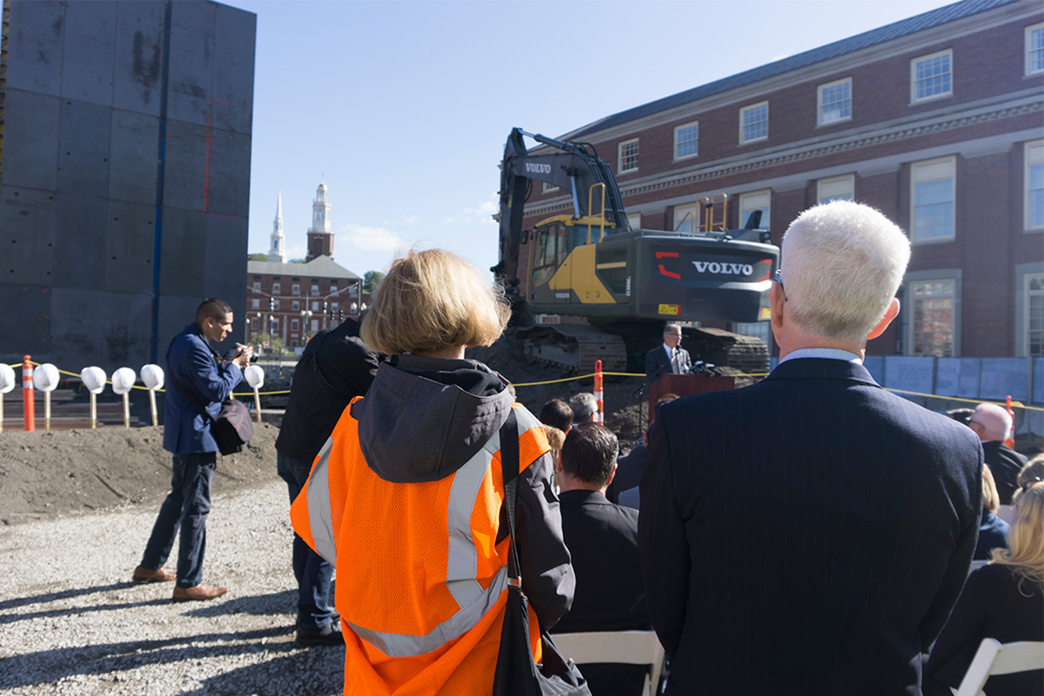 Man giving speech by podium, with over lookers listening-in