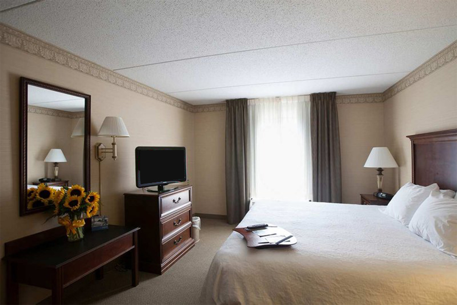 bedroom with large bed, draped windows, and TV on dresser 