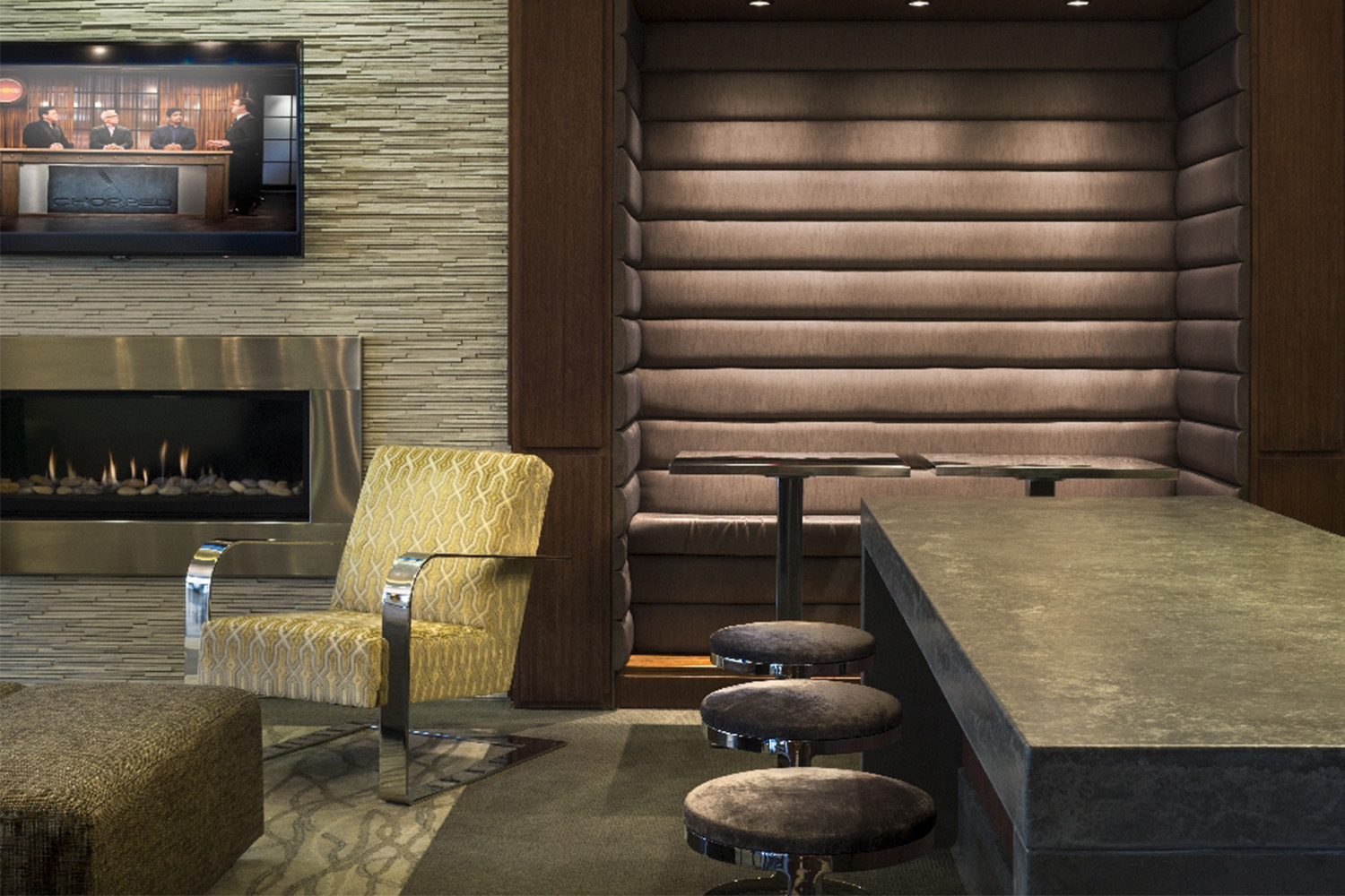 Sophisticated bar area with stools, and a cream chair next to fireplace