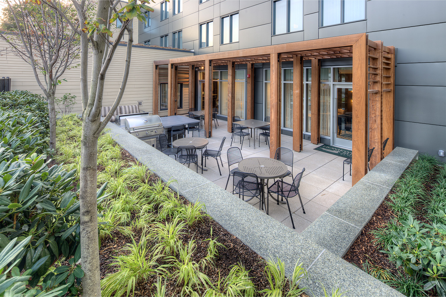 Outdoor patio with grill, metal mesh pullout chairs, and long wooden gateway 