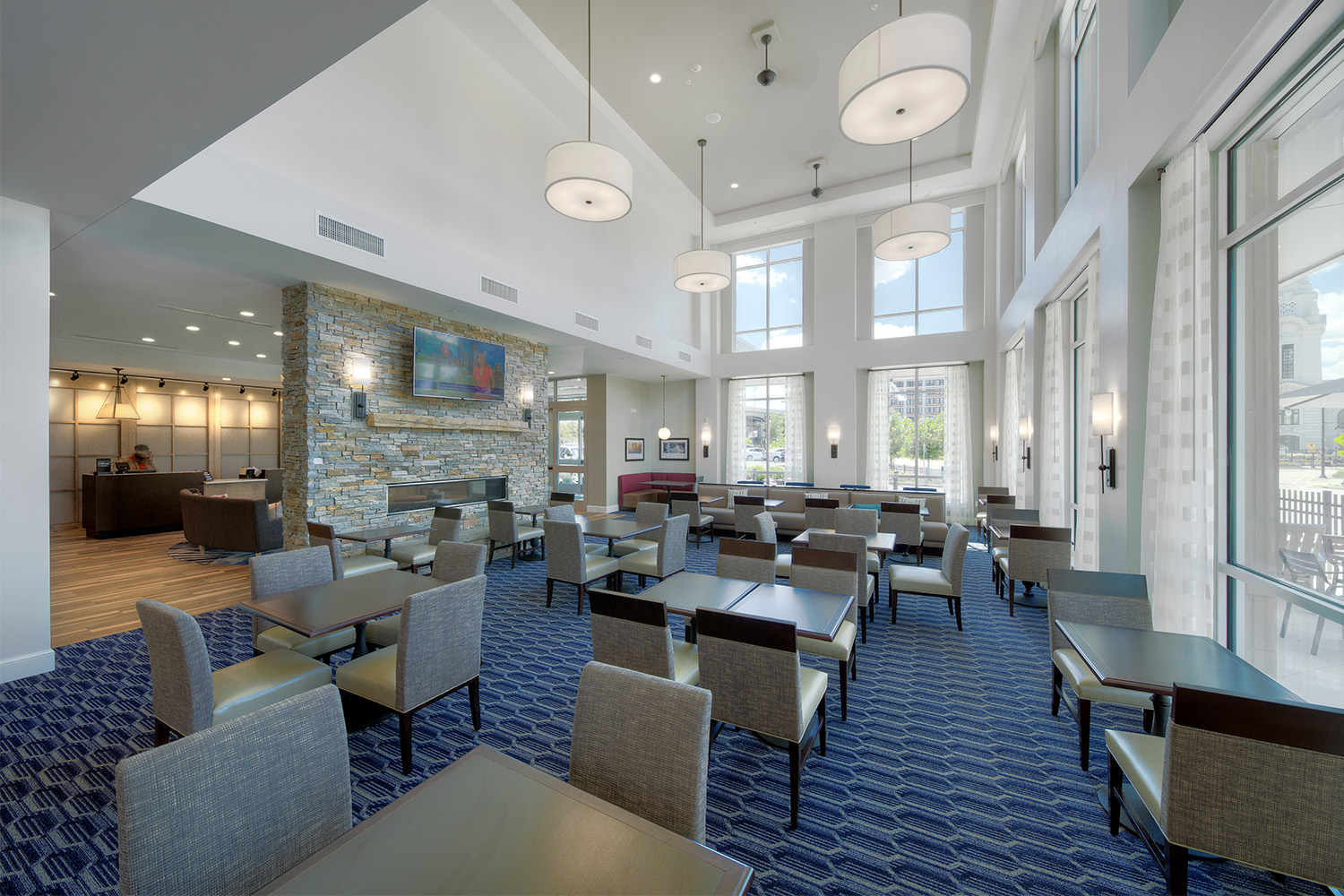 Elegant dining area with tall ceiling, blue carpeting, and various windows allowing ample light in 