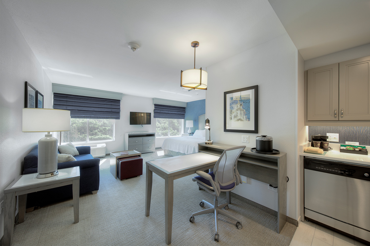 Guest room with dual windows, blue couch, work desk & chair, and plush bed