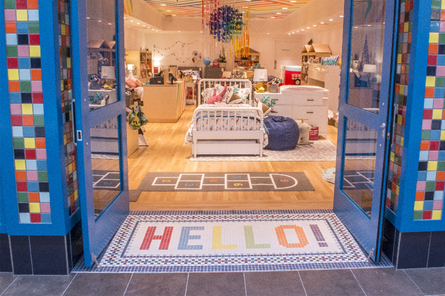 Storefront with colorful tile design next to door, and tiled "HELLO!" at foot of entrance 