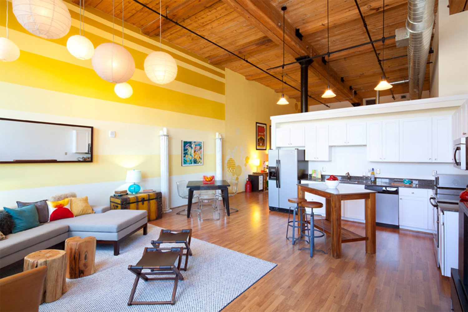 Sleek kitchen with white cabinets, chic living room with pops of color, and an industrial style wooden ceiling 