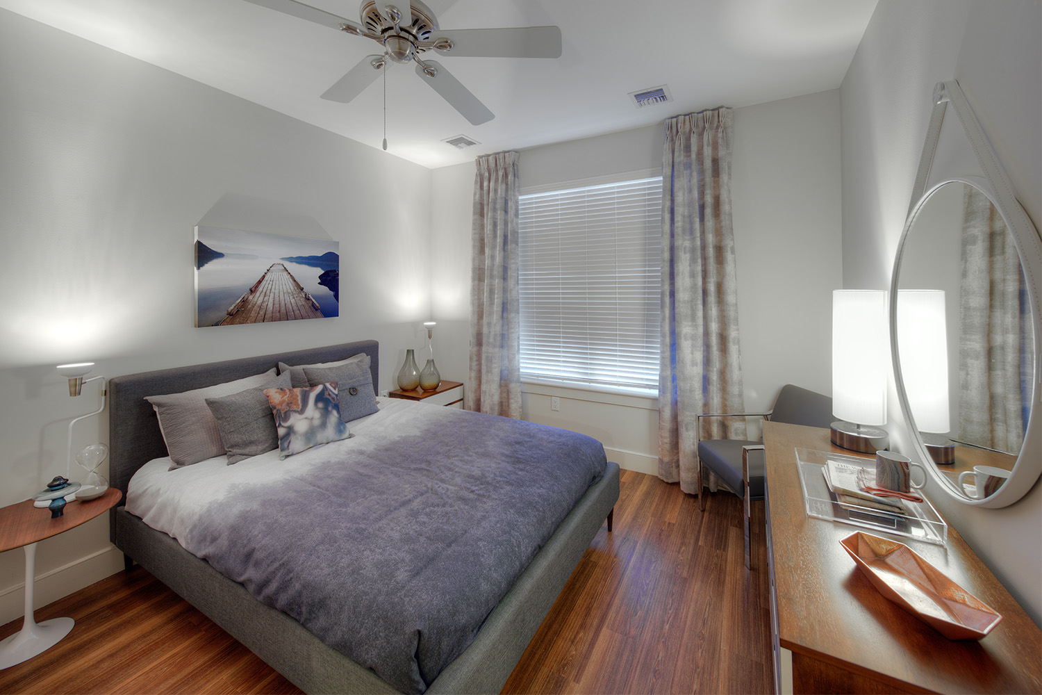 Bedroom with wooden floor, bed with purple sheets, and a drape-covered window 