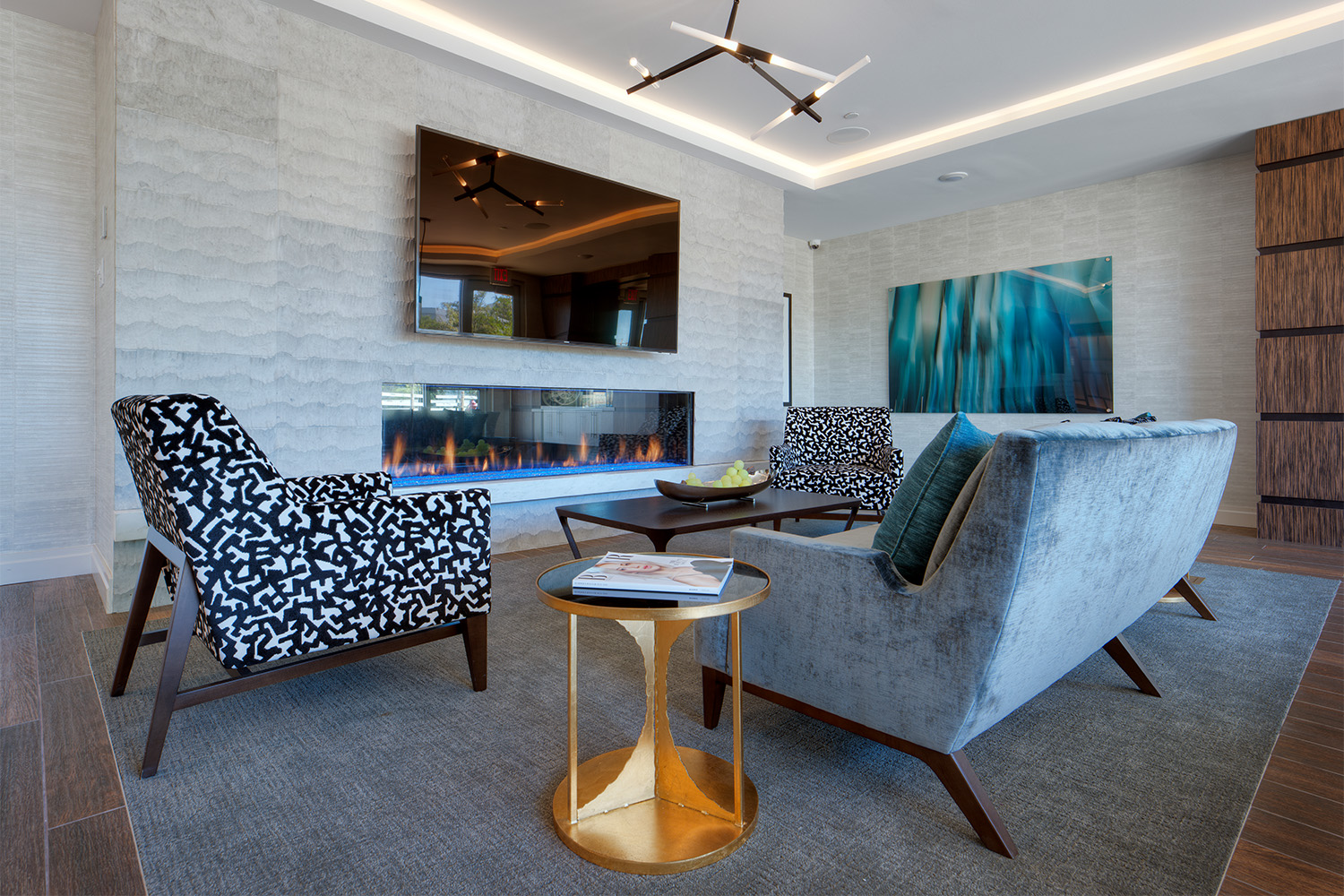 lobby area with 3 plush couches/chairs, in front of TV and faux fireplace