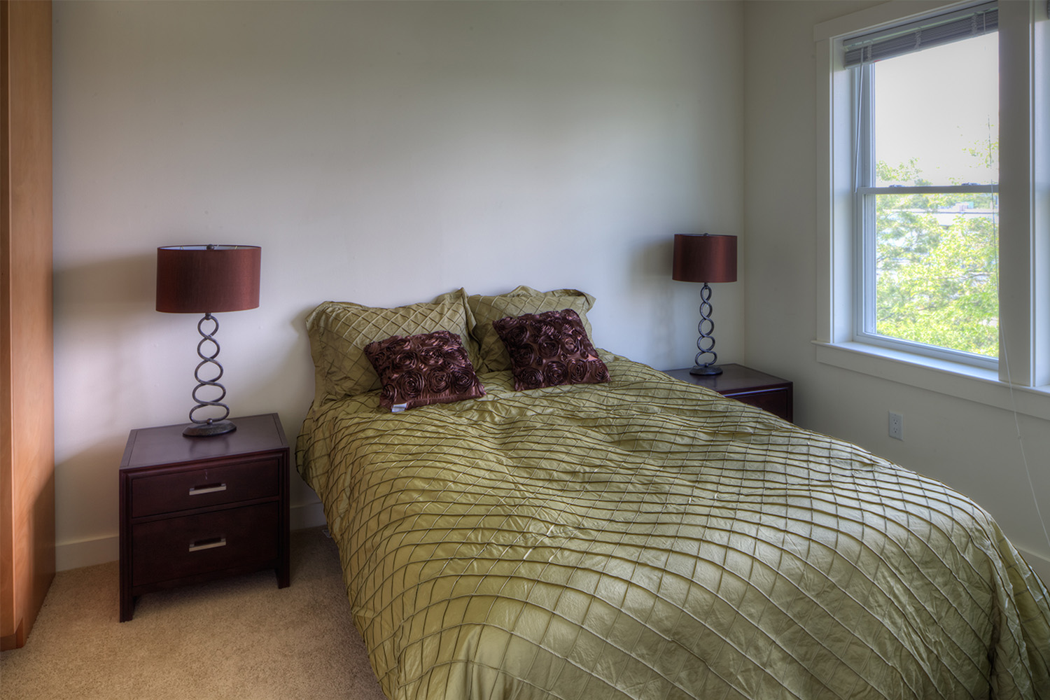 Bed with chartreuse colored blanket, and small window in bedroom 