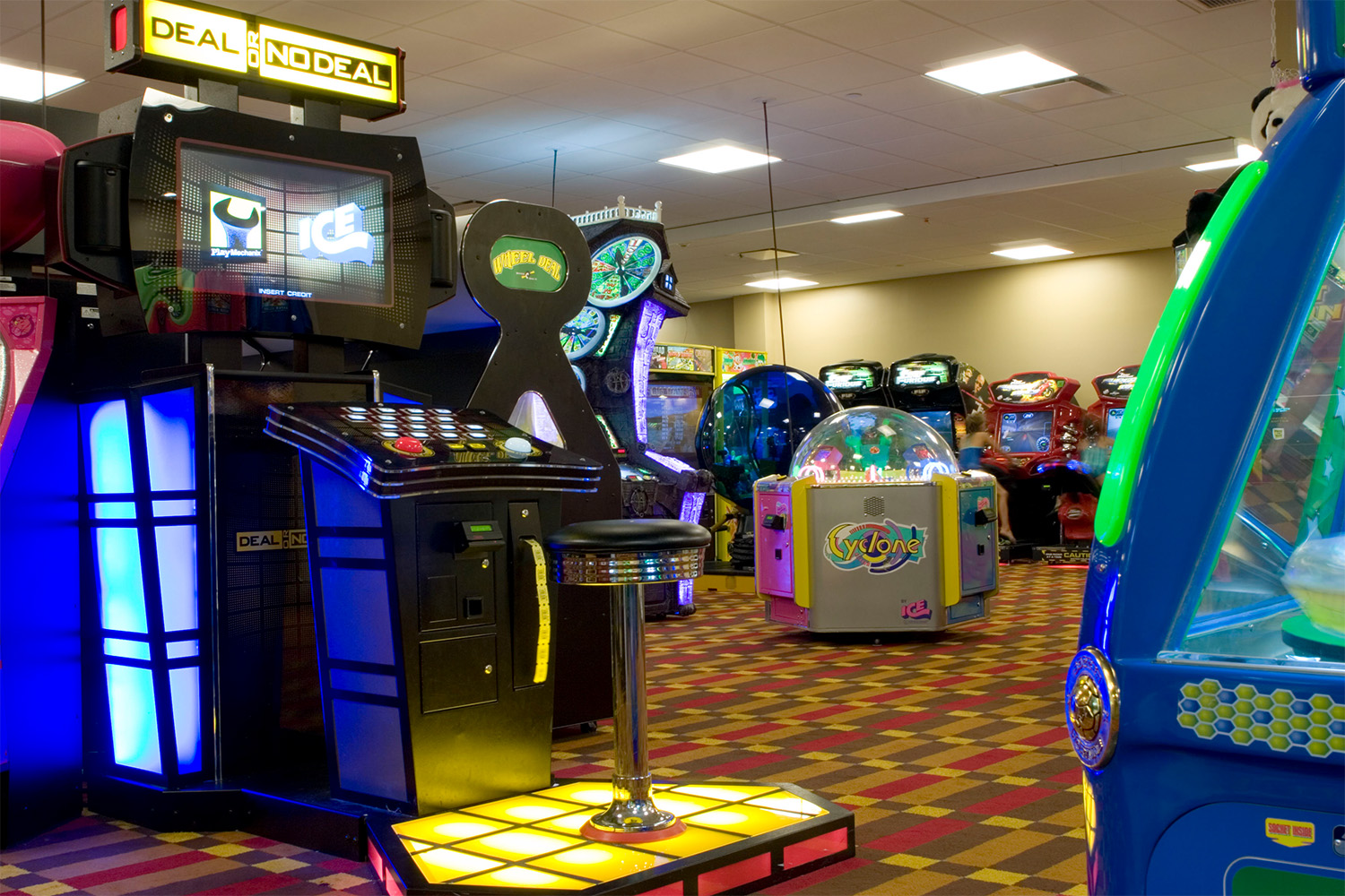 Arcade area with plentiful games, classic public lighting fixtures on ceiling, and carpet flooring