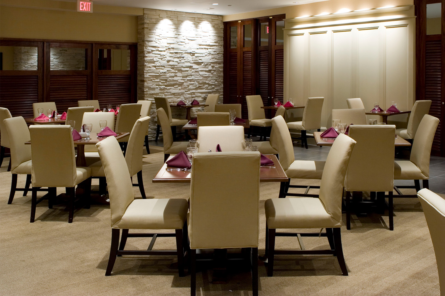 Dining area with tan chairs and wooden tables, and walls comprised of stone bricks and wooden paneling 