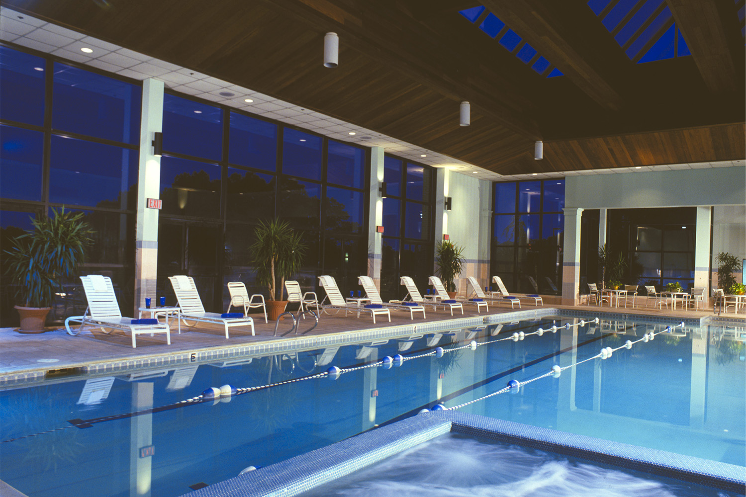 Indoor pool area with wooden ceiling and ceiling windows, and walls comprised of windows 