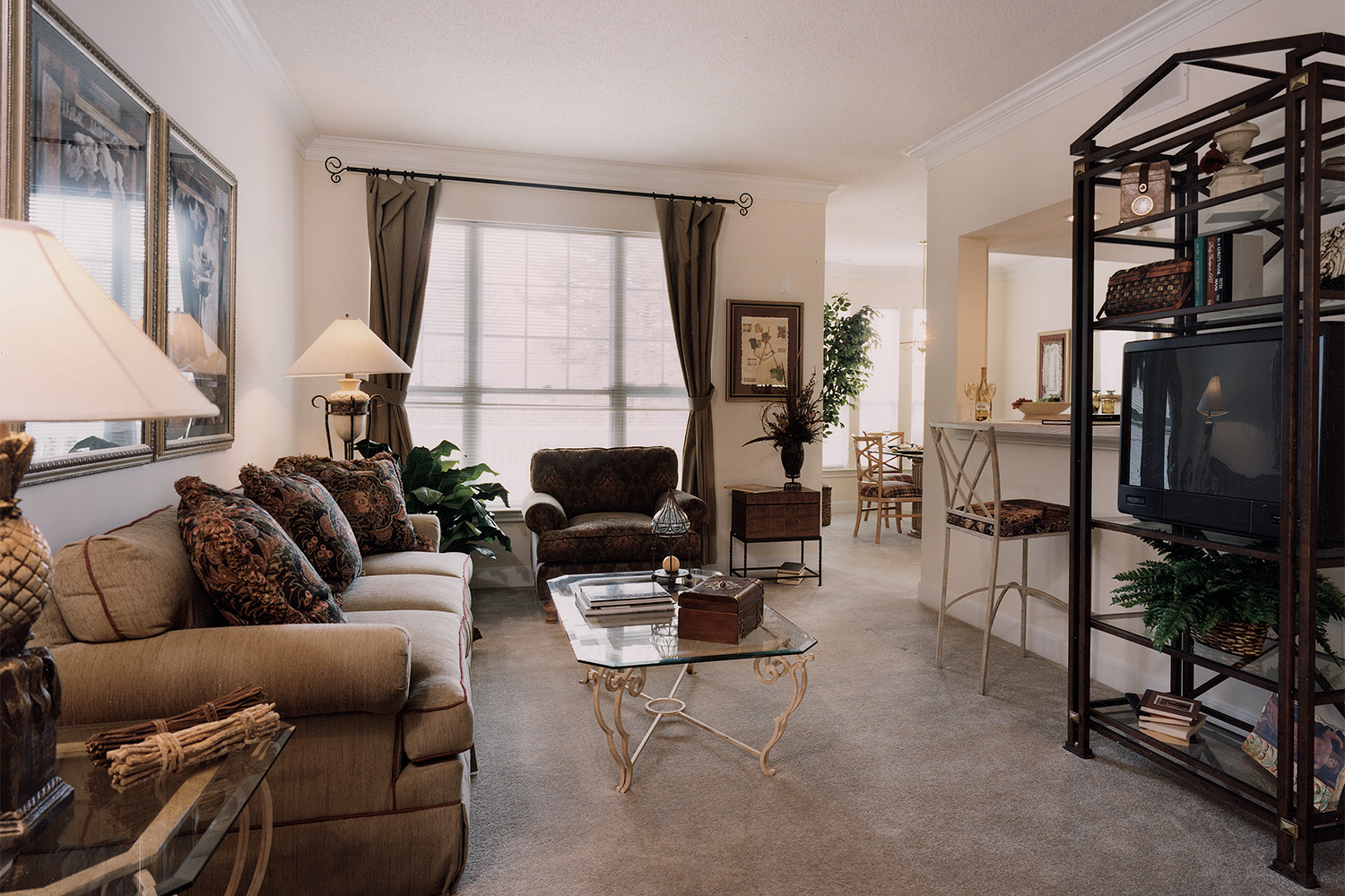 Sideview of living room with large window, glass table, plush tan couch 