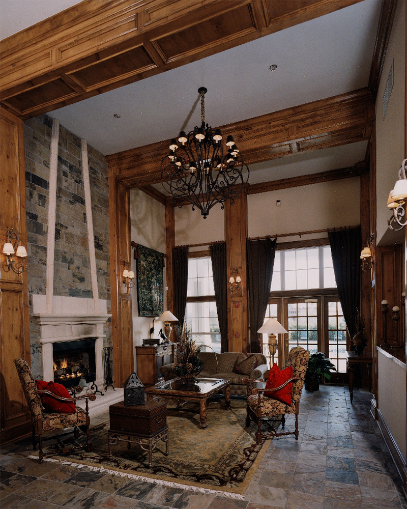 Lobby with exposed wooden beams on ceiling and walls, chandelier, fireplace, and red velvet seating