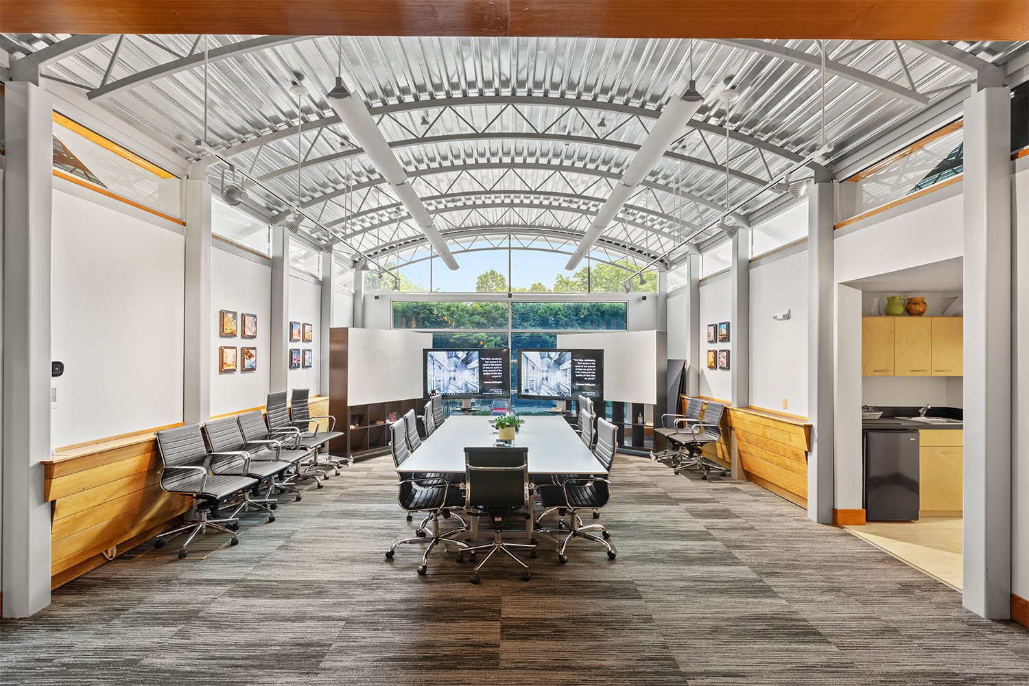 Bright view of TOCCI's lobby conference room, with a main table and two TVs in front of a wall of glass windows.