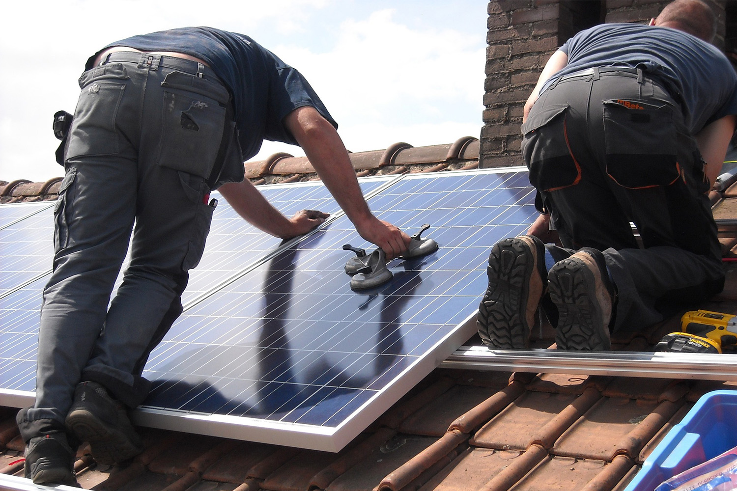 two construction workers installing solar panels onto the roof of a building