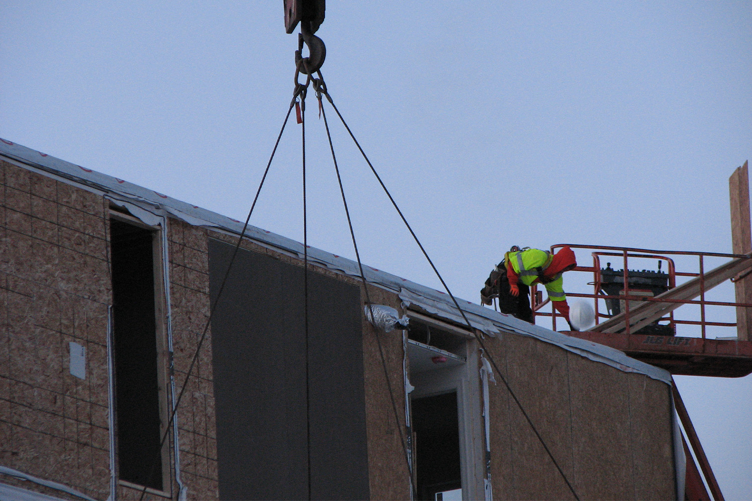 Construction worker on top of a unit being lifted by crane 