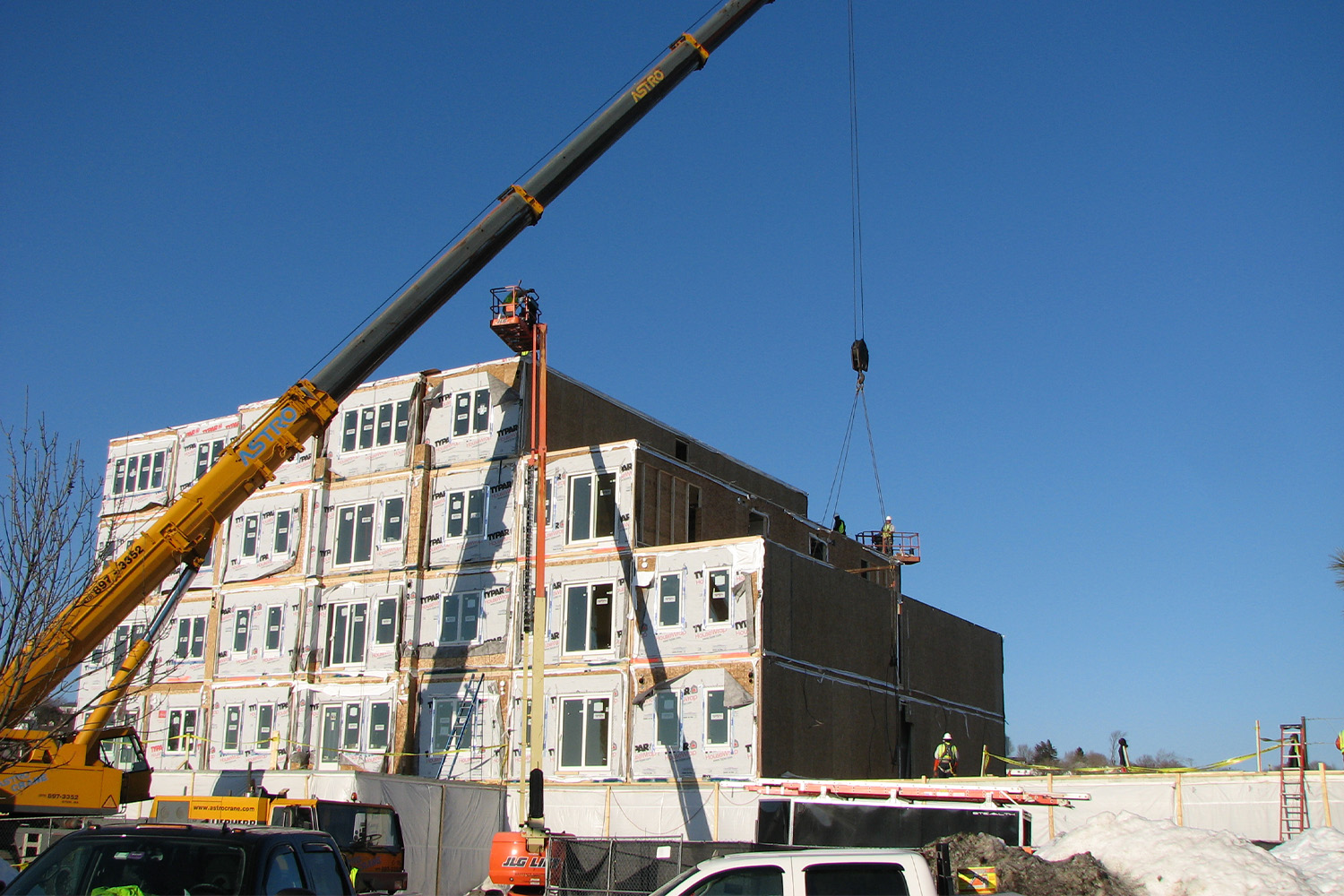 a yellow hydraulic crane lifting a unit to on top of a building 
