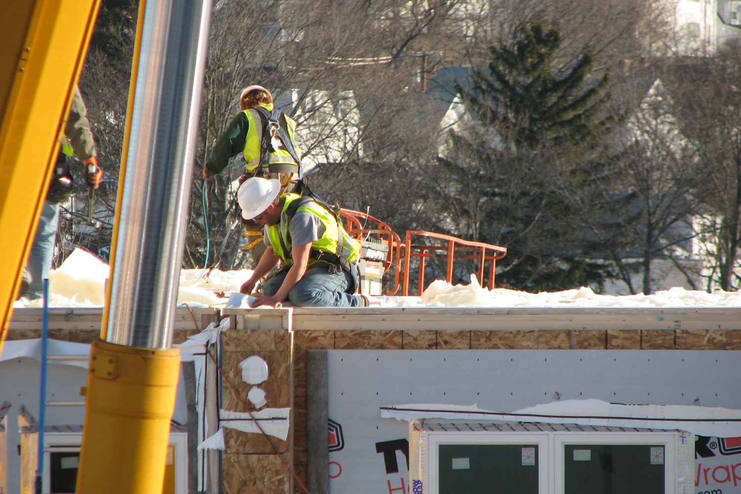 two construction workers in yellow vests, working on a unit roof