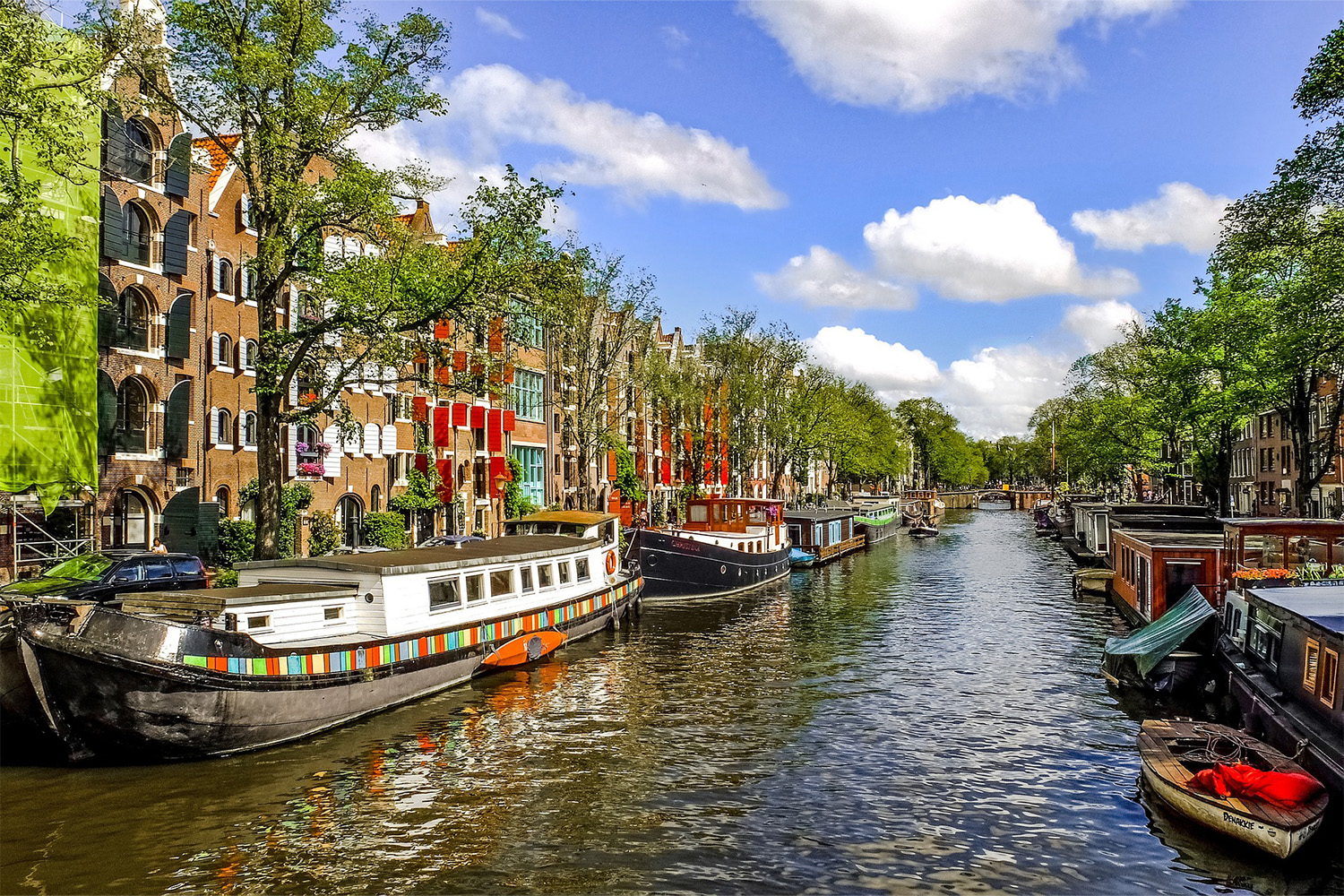 canal in Amsterdam, with multiple colorful boats aligned on both sides 