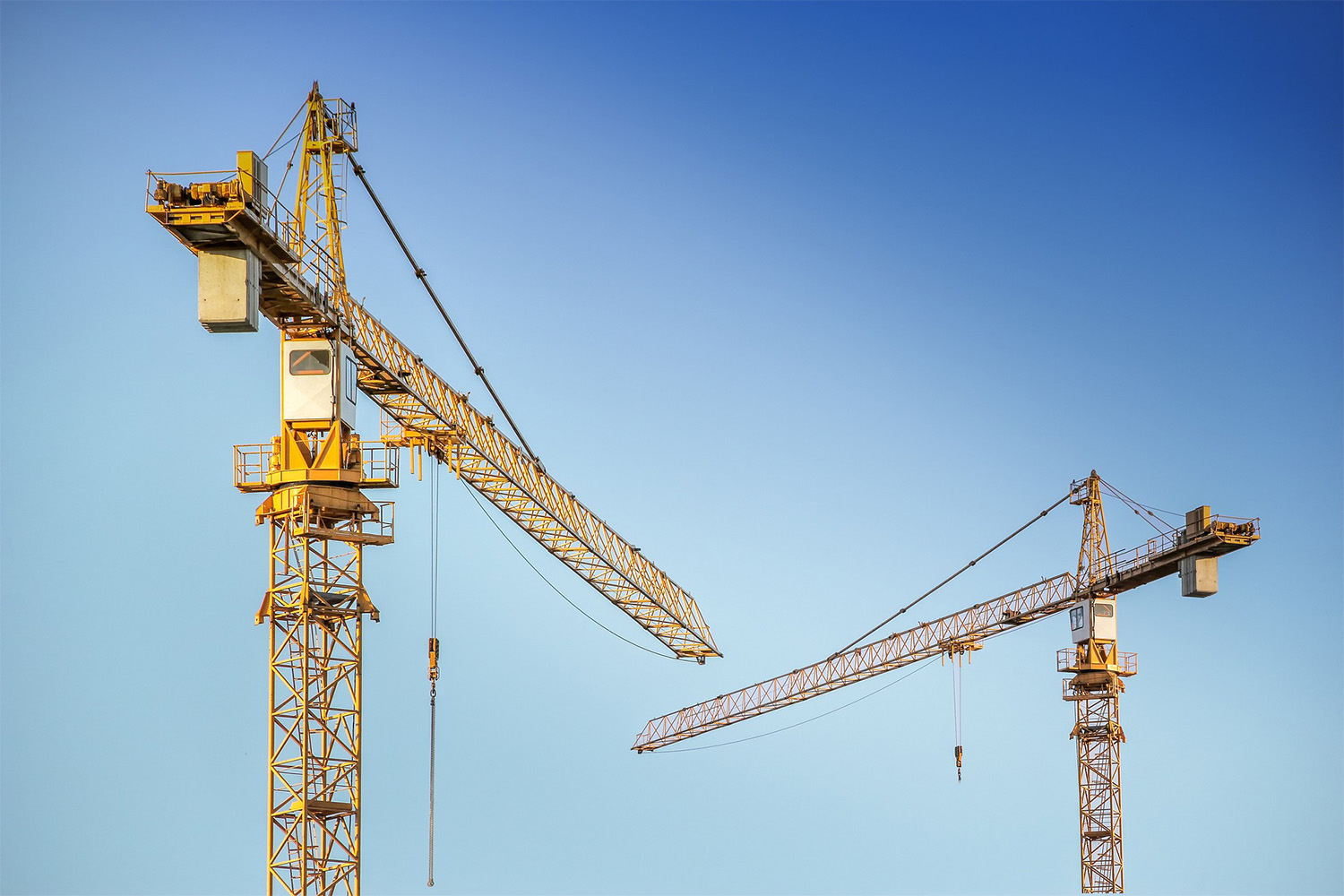 2 cranes used for construction, with blue sky background