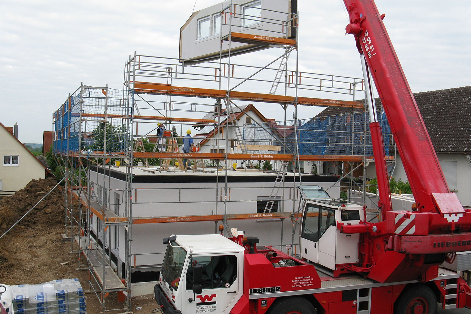 red crane lifting metal beams during construction of apartment complex 