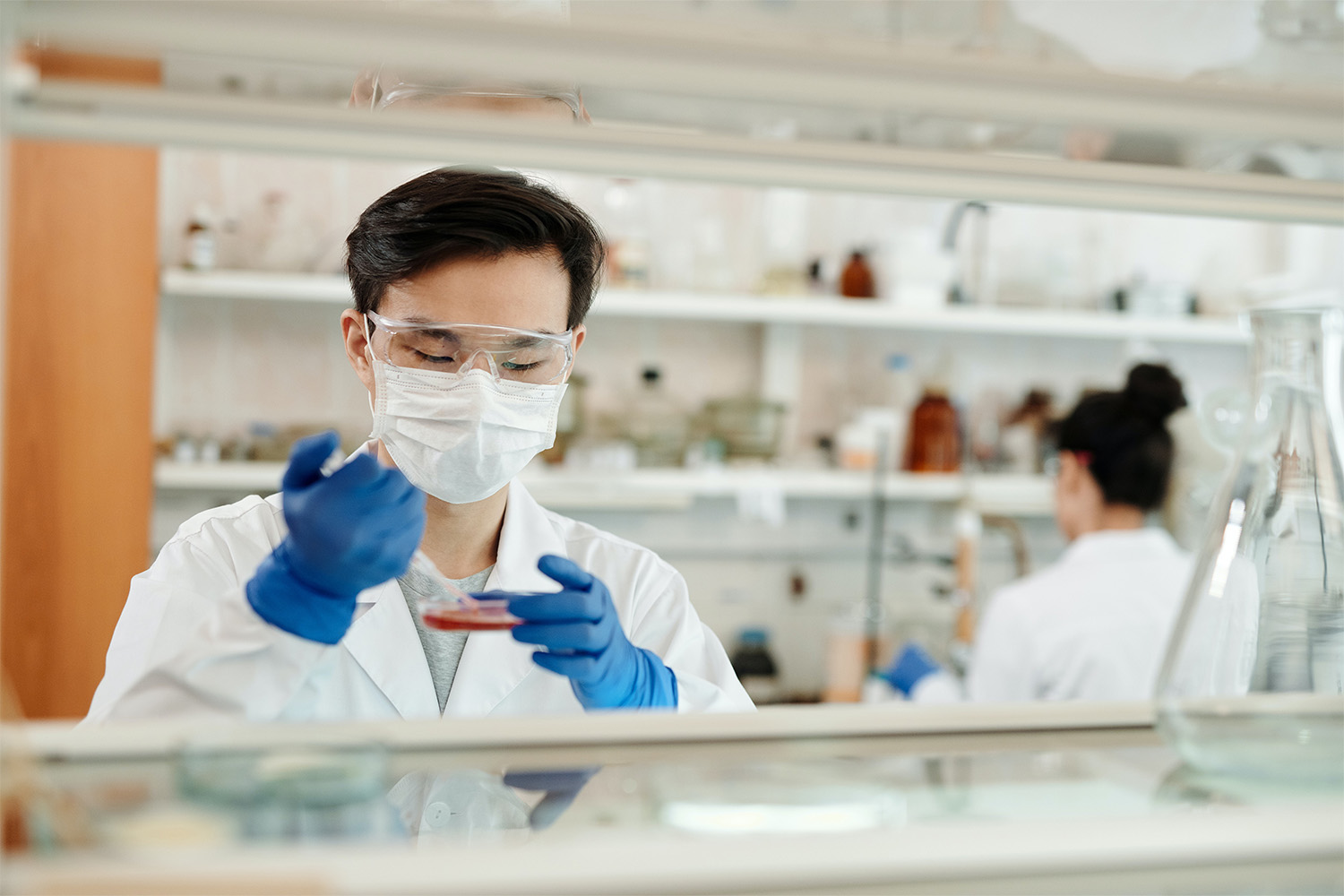 2 people in lab coats, and wearing blue latex gloves 