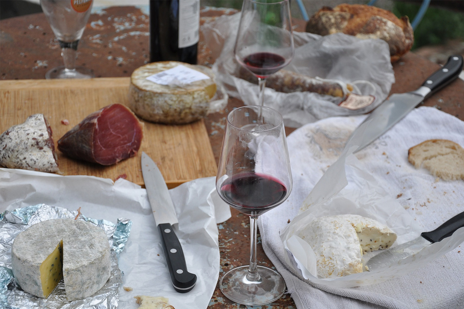 2 glasses with red wine, and various cheeses and cured meats laying around